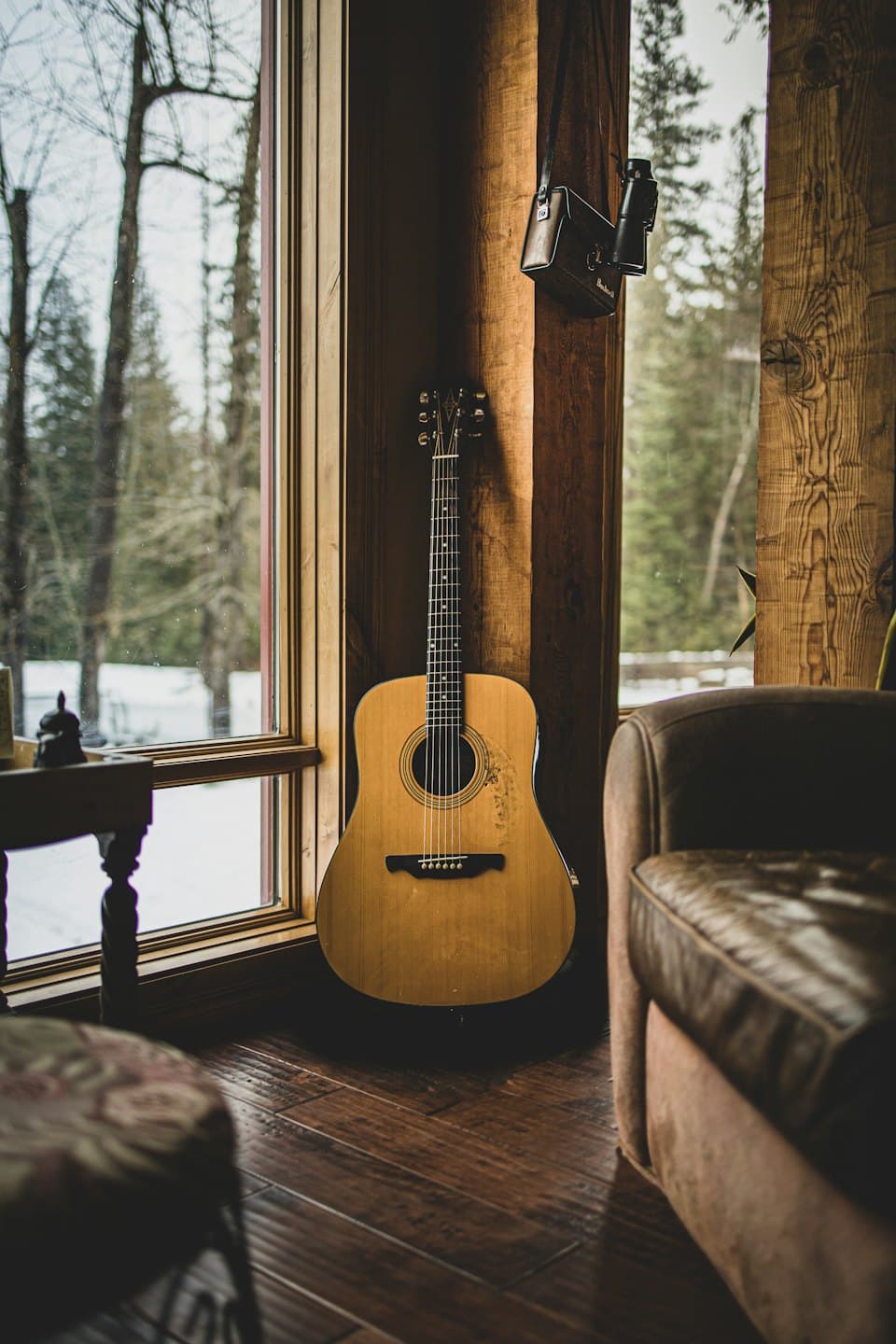 Acoustic guitar standing near a window overlooking a snowy forest.