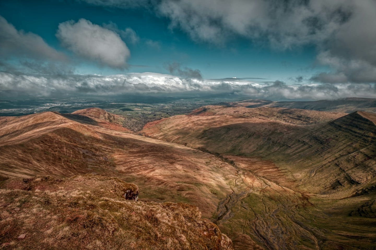 Rolling hills and valleys covered in autumn grass under a partly cloudy sky.