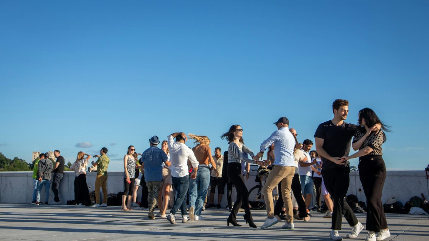 People dance together on a paved outdoor plaza.