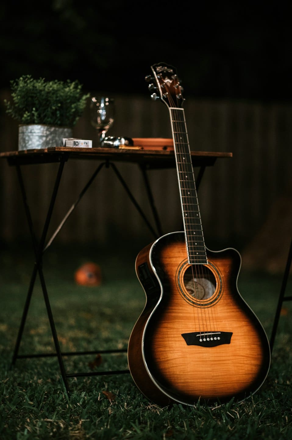 Acoustic guitar leaning against an outdoor table on the grass.