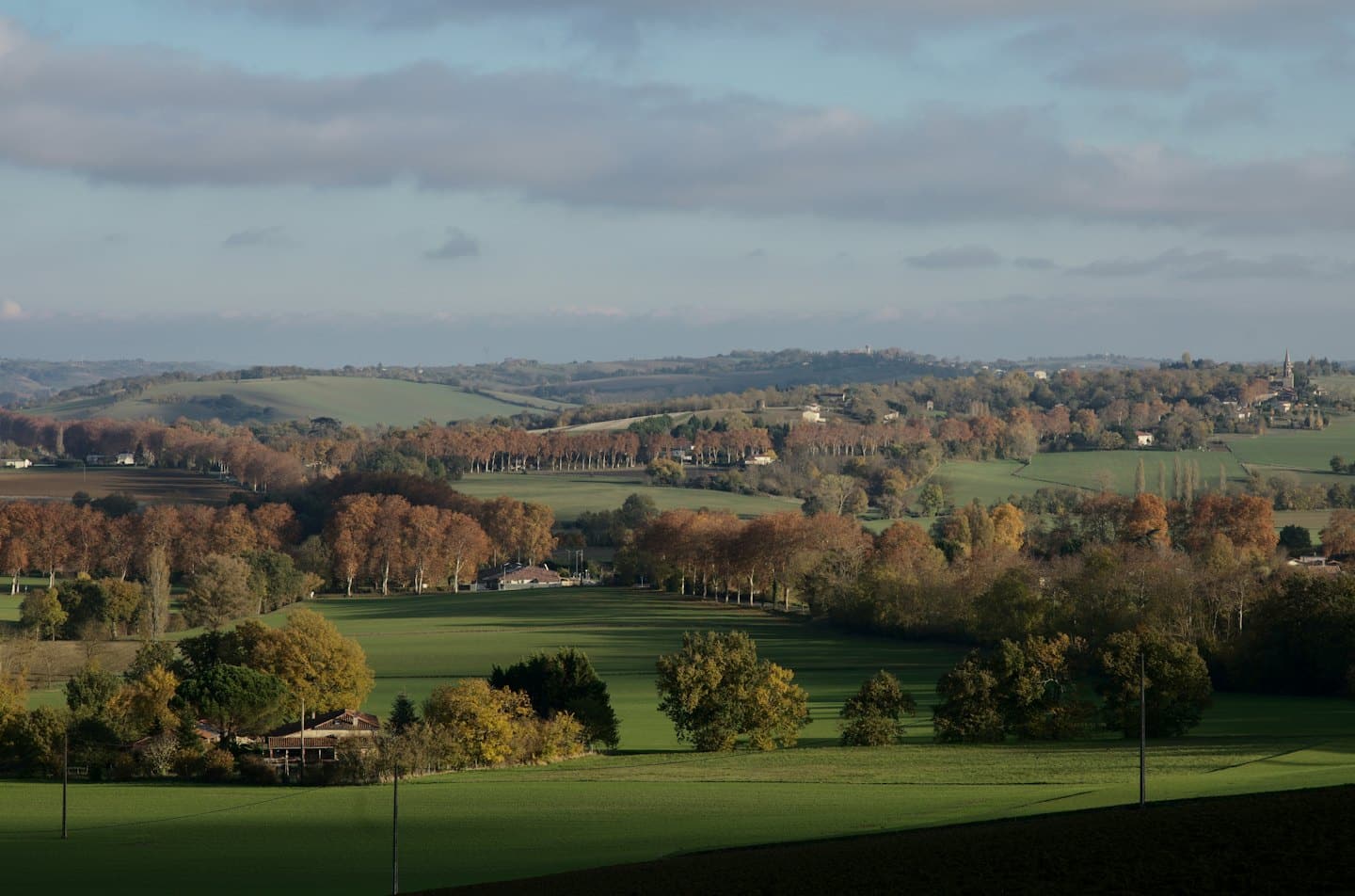 Rolling hills feature green fields and trees with autumn leaves.
